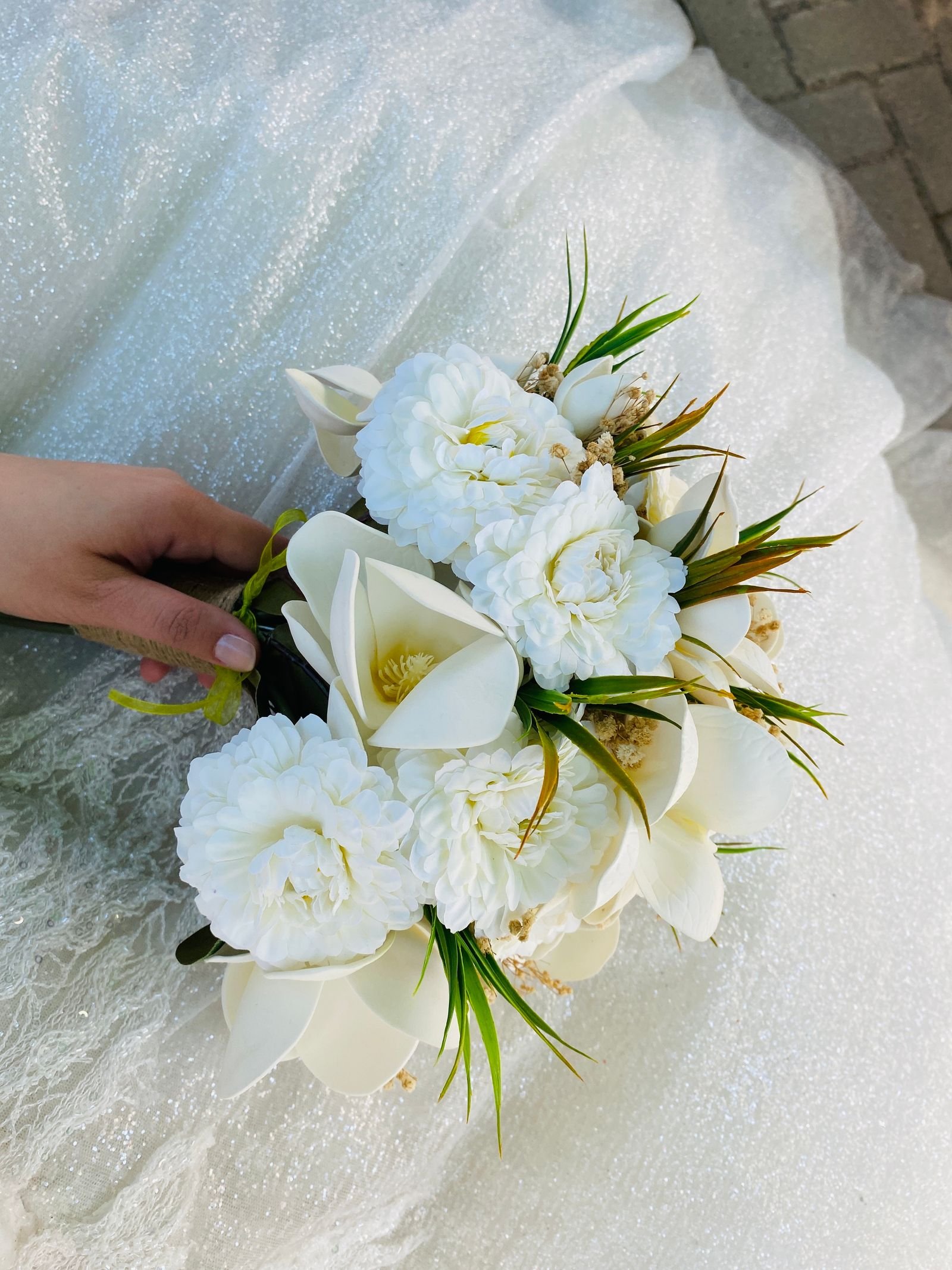 White bridal flowers and greenery held against an ivory dress